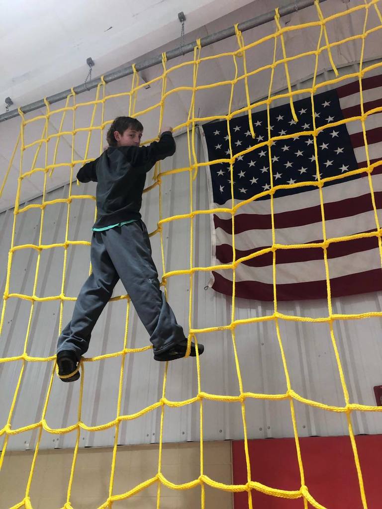 male student climbing yellow net in PE class