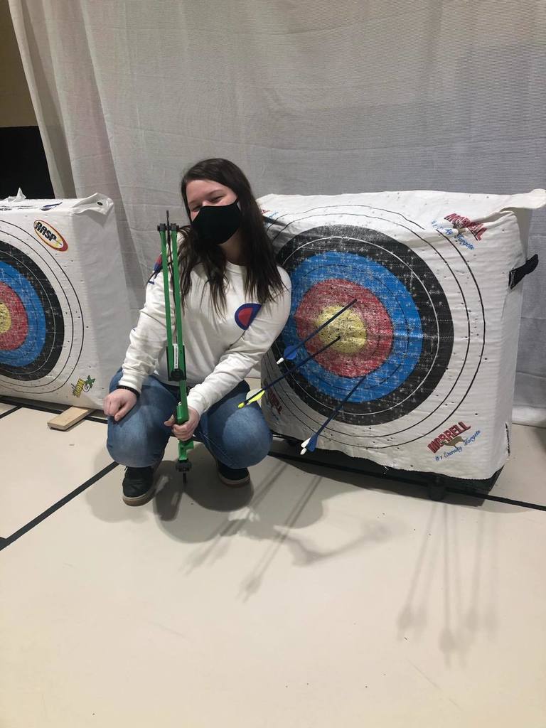 student posing with bow and arrows and blullseye